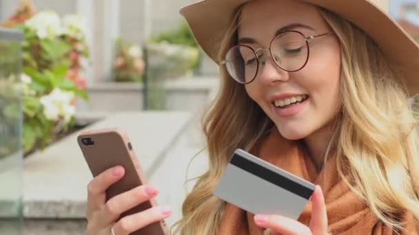 Fiatal lány közelkép, hogy internetes rendelés segítségével telefon boldog nő vásárló kezében telefon és hitelkártya a kezében utcai női ügyfél fogadó cashback online áruház e-banking app szolgáltatás — Stock videók