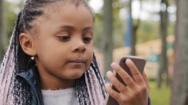 Saçı örgülü, çok ırklı küçük bir kız çocuğu dışarıdaki afro-amerikan çocuğuyla telefon uygulaması üzerinden iletişim kuruyor sevimli bir bebek cep telefonu ekranında elinde bir cihaz tutan kıza bakıyor.