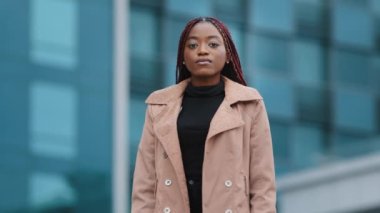 Gerçekten konsantre olmuş, Afro saç stili katlanmış elleriyle dışarıda portresi olan Afro Amerikalı bir kız. Odaklanmış siyah kadın profesyonel ofis binasının arka planında kameraya bakıyor.