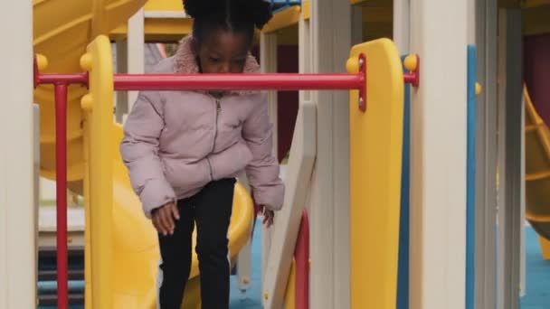 Afrikalı Amerikalı kız tek başına çocuk parkında oynuyor merdivenlerden atlıyor ve aşağı kayıyor. Çocuklar, çocuklar, okul çıkışları, açık hava yürüyüşleri. Mutlu çocukluk tatilleri. — Stok video