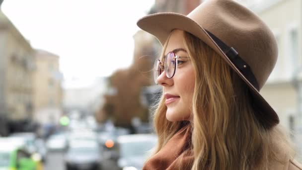 特写白俄罗斯女学生吸引人的年轻女子想站在城市女士的大街上，沉思地看着远方的边景千年金发女郎，戴着帽子和眼镜 — 图库视频影像