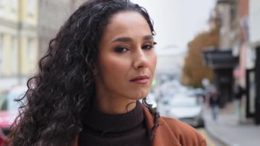 Düşünceli, genç, güzel, güzel, esmer, kadın model turist şehrin caddesinde durup kameraya bakıp gülümseyen, sağlıklı dişli, samimi, samimi bir gülümseme takınıyor.