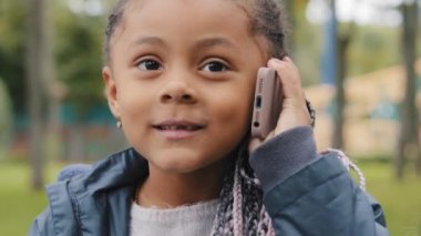 Cep telefonuyla konuşan küçük bir kız. Çok ırklı bir çocuk. Kameraya bakıyor. Telefonlara bakıyor.
