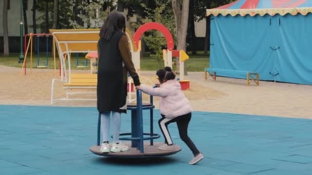 Jonge vriendelijke familie wandelen op speeltuin klein meisje draait moeder op carrousel kind snel ritten gelukkig jeugd hebben plezier samen moederschap vreugde vrolijk klein kind op vakantie besteedt tijd met mam — Stockvideo