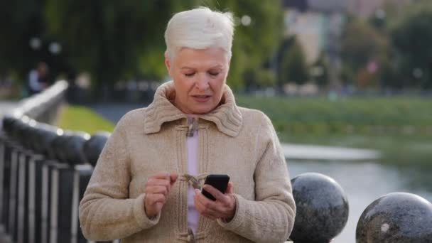 Сверхрадостные счастливые седые волосы зрелая женщина держит смартфон читать смс уведомление отличная новость выглядит взволнованной не могу поверить, что удача наслаждаться моментом победы весело с мобильного устройства. Концепция успеха — стоковое видео