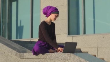 Aşırı çalışmaktan yorgun düşmüş Müslüman kız iş kadını şehirde oturup laptopta çalışıyor bilgisayarın Lotus pozisyonunda oturup meditasyon yaparken kızgın hissediyor.