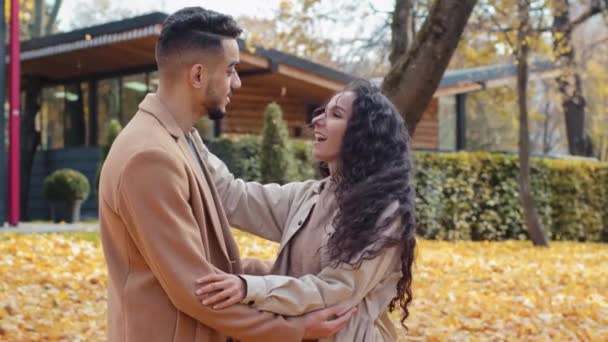 Španělština šťastný pár v lásce stojící venku pohledný muž a žena s kudrnaté vlasy zábava komunikovat v podzimním parku chlap bod s rukou vousatý španělský muž objímání žena krásná bruneta úsměv — Stock video