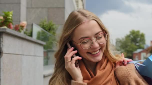 Close-up gelukkig meisje lopen op straat aantrekkelijk jonge vrouw geniet van mobiele telefoon gesprek Kaukasische vrouwelijke klant met draagt heldere boodschappentassen met aankopen buiten antwoorden oproep bellen — Stockvideo