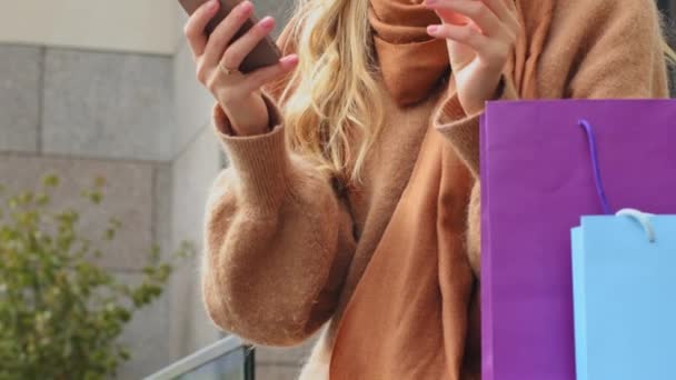 İnternet üzerinden alışveriş yapan mutlu bir kız. Elinde kredi kartı ve akıllı telefon olan genç bir kadın. Açık havada market paketleriyle oturuyor. — Stok video