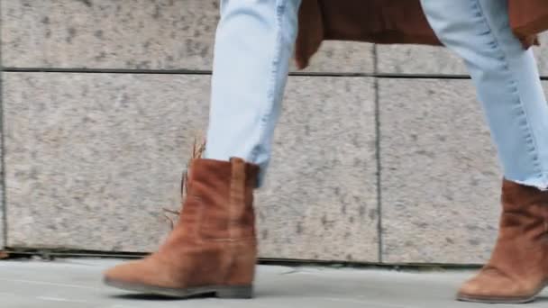 Detailní záběr ženských nohou kráčejících po chodníku ve městě. Oříznutý pohled na nepoznatelnou ženu v modrých džínách a hnědé stylové módní boty jít na ulici pohybující chůze, módní koncept — Stock video
