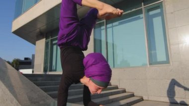 Pincha Mayurasana açık havada dengede duruyor. Hareket eden Müslüman kız tesettüre girmiş, yoga yapan yoga yapan yoga yapan, akrobatik kol kasları ön kol ve bacaklarda ağırlık yapıyor.