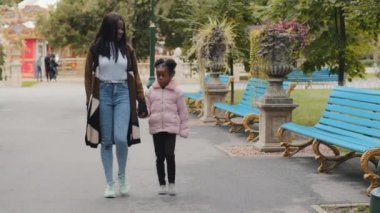 Genç bir anne kızını kucaklıyor. Mutlu bir Afro-Amerikan ailesi. Şehir parkında yürüyen bir çocuk.
