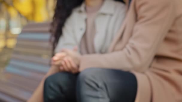 Närbild suddig oigenkännlig ung par sitter på bänk i staden höstpark pojkvän kramar lockigt flickvän kärlek partners hålla händer datum utomhus njuta av tid tillsammans relation koncept — Stockvideo