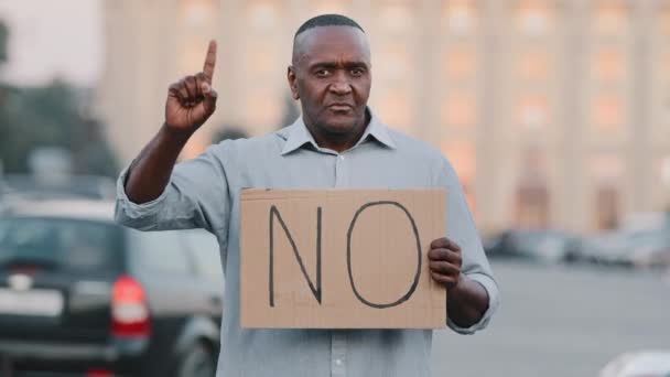 Черный иммигрант, держащий картонный лозунг с надписью "нет", афроамериканец, стоящий в городе, не согласен с отказом от вакцинации. Остановить расистскую дискриминацию — стоковое видео