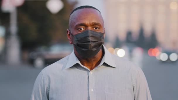 屋外でポーズをとる黒い保護医療面マスクを身に着けている成人のアフリカ系アメリカ人男性。パンデミック時の路上に立つ高齢者のビジネスマンcovid-19 、ウイルス保護、コロナウイルスの流行 — ストック動画