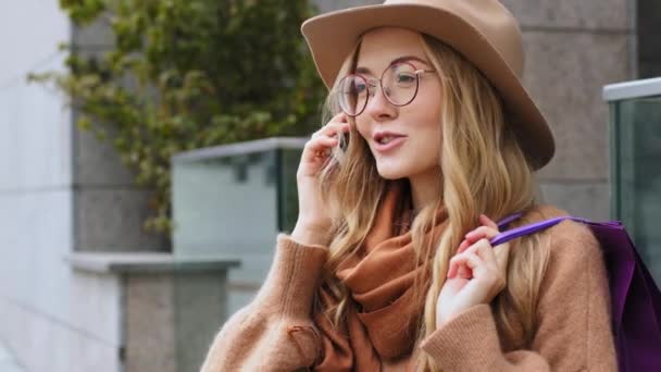 Retrato chica joven contesta felizmente llamada telefónica atractiva hembra comprador de pie en la calle en la ciudad celebración de paquetes de compras señora caucásica comunicarse utilizando móvil millennial mujer sonriendo al aire libre — Vídeos de Stock