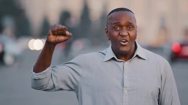 Уверенный пожилой черный мужчина социальный этнический активист говорит на открытом воздухе делает жест да держит кулак в воздухе сила единства знак гордости символ, афроамериканский бизнесмен предприниматель радуется триумфу — стоковое видео