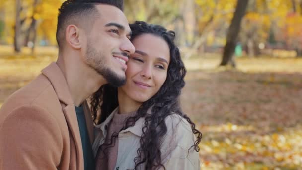 Dreamy arabic couple looking into distance outdoors partners in love enjoy spending time together attractive guy tight hug beautiful curly woman in autumn park amorous close relationship smiling pair