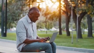 Yaşlı Afro-Amerikan adam dışarıda oturuyor modern cihazda kablosuz internete bakıyor, dizüstü bilgisayarda mesaj yazıyor, yetişkin serbest yazar müşteriye danışmanlık yapıyor, teknoloji konsepti