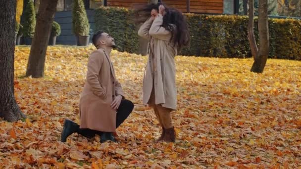 Spaanse liefdevolle paar in de herfst park man staan in gele bladeren op een knie maken huwelijk aanzoek vriendin en zet ring aan vinger opgewonden gelukkig vrouw springen en strak knuffels lieverd man buiten — Stockvideo