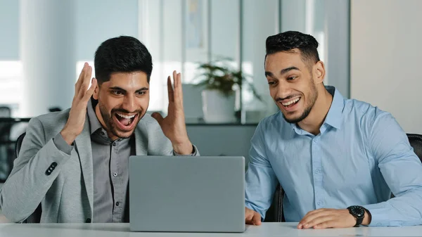 Two Arab young male businessmen sitting in modern office using laptop employees satisfied with result of negotiations, having concluded contract, Indian colleagues receiving good news feeling thankful — Stock Photo, Image