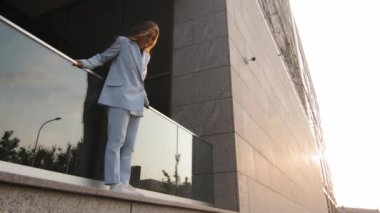 Üzgün stresli kadın, şık mavi takım elbiseli, yalnız kadın, yükseklerde, teras balkonunun korkuluklarında duran intihar sorunu kavramının düşme tehlikesine bakıyor.