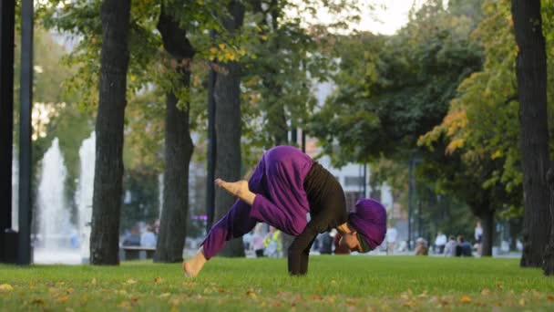 Forte ragazza musulmana attiva in hijab donna yogi sportiva che fa allenamento di yoga nel parco sul prato verde facendo equilibrio handstand formazione tenendo gamba in aria elemento acrobatico si muove attivamente stretching asana — Video Stock