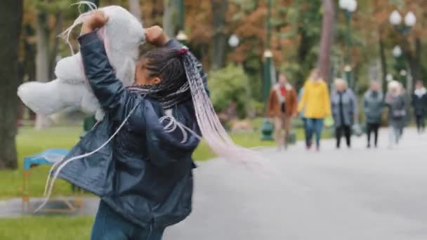 Klein schattig meisje spelen in het stadspark Afrikaans kind wervelend rond houden teddy beer afro-Amerikaans kind spel gelukkig buiten spelen in het weekend schoolmeisje lopen na school springen vrolijk glimlachen — Stockvideo