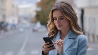 Portre ciddi odaklı güzel beyaz kız iş kadını şehrin arka sokaklarında duruyor cep telefonuyla sohbet ediyor internet üzerinden akıllı telefonlu uygulama alışverişi yapıyor.