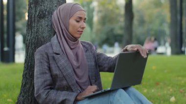 Başörtüsü içinde yorgun bir kız öğrenci. Bilgisayarı olan genç bir iş kadını. Yeşil çimenlikte, ağaçların yanında oturuyor.