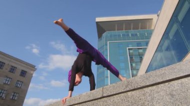 Şehirde tesettürlü Müslüman bir kadın yoga yapıyor amuda kalkma egzersizi yapıyor hava kuvvetlerinde denge sicimi deniyor. Sokak modern bina arka planında güçlü kadın aerobik sporu Asana