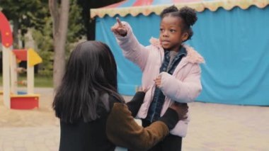 Çocuk parmakla işaret eden anne kendine iyi bak çocuk anne başını çeviren küçük kız oyun parkında annesiyle aktif olarak iletişim kuruyor Afro-Amerikan aile eğlencesi anne ve bebek dışarıda gülümseyerek vakit geçiriyor.