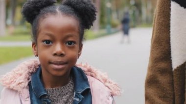 Mutlu çocuk yürüyüşünü tamamla. Parktaki anne ve kızıyla birlikte mutlu bir şekilde gülümse. Kameraya bakıp Afro-Amerikan ailesini izle.