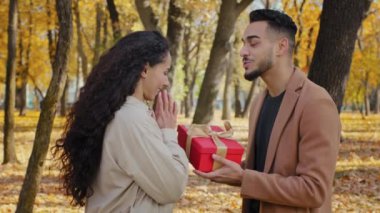 İspanyol yakışıklı sakallı adam hediyesini altın kurdeleli büyük kırmızı bir kutuya veriyor. Sonbahar parkında çekici genç bir kadın. Kız arkadaşına sarılıyor.