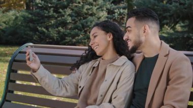 İspanyol çift, sonbahar parkında akıllı telefon kullanıyor. Kız ve erkek el sallıyor. Merhaba genç aile.