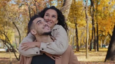 Sonbahar parkında buluşan İspanyol çift mutlu bir şekilde gülümsüyor çekici kız omuzlarından erkek sarılıyor yakışıklı sakallı adam sırtında bir kadın ile geziyor güneşli sonbaharın keyfini çıkarıyor.