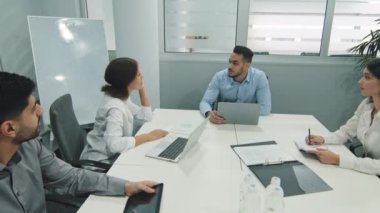 Konferans masasında oturan iş adamları. Kendine güvenen Arap işadamı iş arkadaşları veya ortaklarıyla konuşuyor, erkek lider toplantıda veya görüşmelerde müşterilerle sohbet ediyor