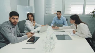 Genç Hintli takım lideri iş arkadaşlarıyla oturup müzakere toplantısında sorunları tartışıyor. Başlangıç pazarlama stratejisini geliştirmek için ofiste birlikte çalışan yetenekli bin yıllık çeşitli çalışanlar.