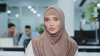 tesettürlü gülümseyen Arap müslüman kadın şirket çalışanı röportaj yapıyor, kameraya bakıyor. Doğulu bayan girişimci genç üst düzey yönetici ya da sözleşmenin şartlarını açıklayan başarılı işçi