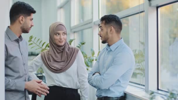 Tres colegas profesionales diversos que hablan en la oficina moderna, mujer musulmana árabe amistosa feliz en hijab y dos compañeros de trabajo indios de los hombres que tienen conversación discuten proyecto de negocio en el espacio de trabajo — Vídeos de Stock