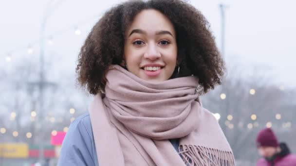 Portrait of young mixed race girl with curly hair in outerwear with pink scarf stands on street in city outdoors looking at camera smiling exhales steam in cold weather in winter enjoys autumn season — Stock Video