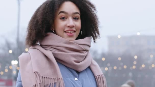 Portrét mladé stylové smíšené závod dívka v outwear africký Američan žena s kudrnaté vlasy stojí ve městě na ulici otáčení kolem při pohledu na kameru s úsměvem zubatý upřímný zubař těší zimní čas — Stock video