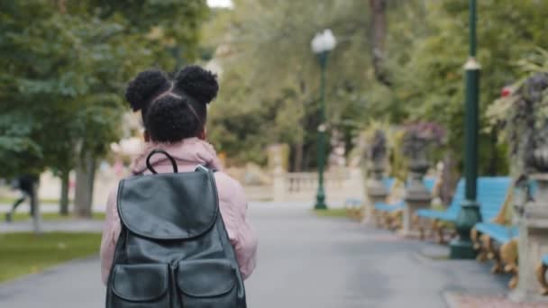 Вид сзади Маленькая афро-американская девочка африканский ребенок черный ребенок с рюкзаком бежит спешит в школу. Концепция образования. Маленькая школьница бегает на свежем воздухе в городском парке, ходит на занятия после урока — стоковое видео