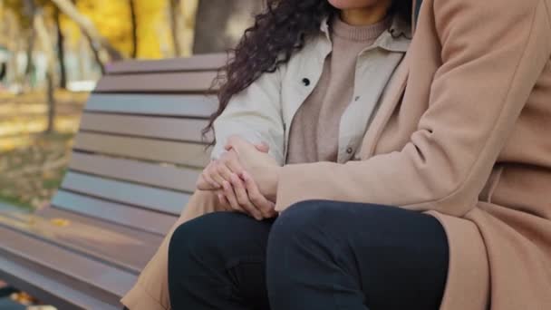 Primer plano joven pareja cogida de la mano sentado en el banco chico gentilmente abraza chica amantes irreconocibles disfrutar de fin de semana en otoño parque romántico cita novio y novia al aire libre fuerte concepto de relación — Vídeos de Stock