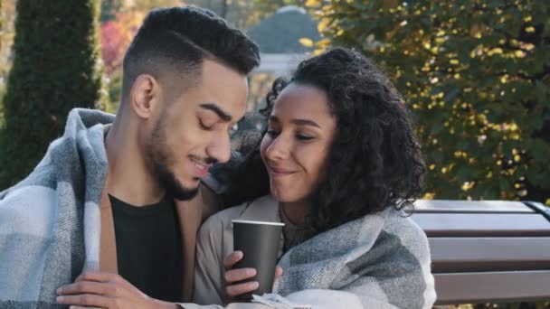 Radosna Latynoska para uśmiechnięta pokryta kratą na randce w jesiennym parku na ławce młoda dziewczyna pije kawę dba o chłopaka prostowanie koc facet przytulić ukochaną dziewczynę mężczyzna i kobieta rozmowa — Wideo stockowe