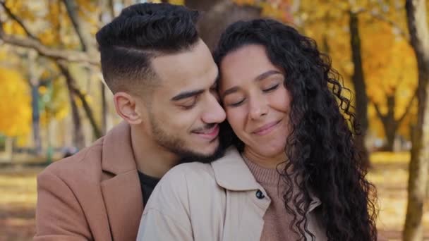 Hispanic couple cuddling outdoors girl and guy on romantic date in autumn park family look into each other eyes lovers enjoy gentle embracing man and woman touching cheeks close-up beloved fun smiling — Stock Video