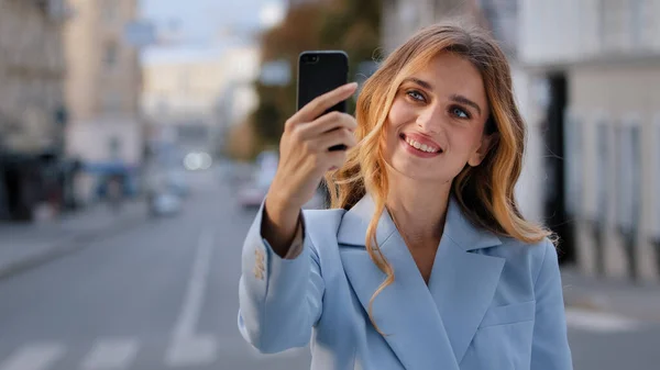 城市里年轻美丽的高加索女孩商业女性博主维基百科模特儿的肖像站在城市里，手持手机，用手机在线聊天，为博客拍照 — 图库照片