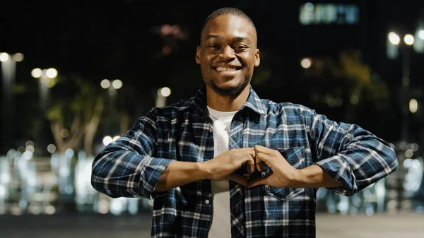 Afro american man african guy standing in night city affectionate romantic portrait looking at camera make heart shape with fingers. Lovely boy showing love kindness tenderness support sign with hands — Stock Photo, Image