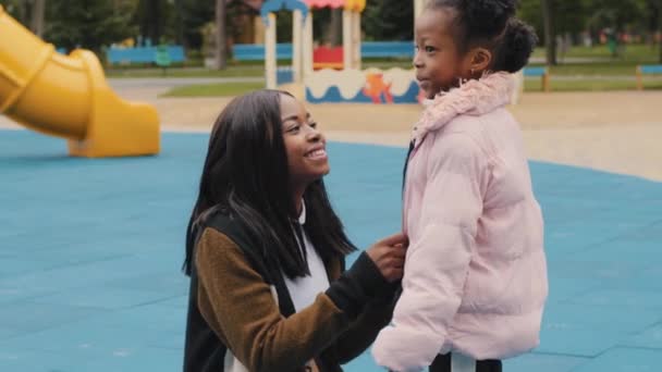 African American young mother care of little daughter family relationship happy afro child with attractive mom spend time together on playground in park szczere macierzyństwo prostuje ubrania dla dzieci — Wideo stockowe