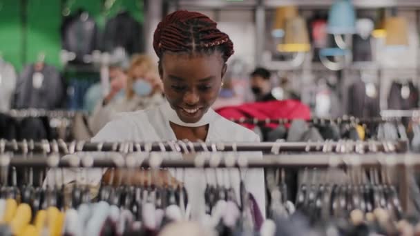 Joven mujer afroamericana elegante comprador consumidor en la tienda de ropa del centro comercial elige el equipo en busca de ropa hermosa encuentra chaqueta se ejecuta a través de rack de sonriente hallazgo satisfecho — Vídeos de Stock
